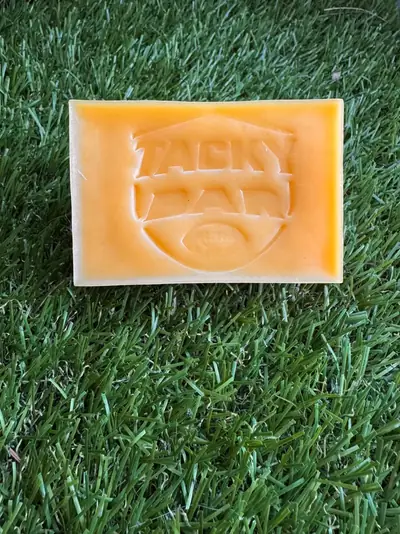 Top view of a Tacky Bar on turf, the shield logo pressed into the wax
